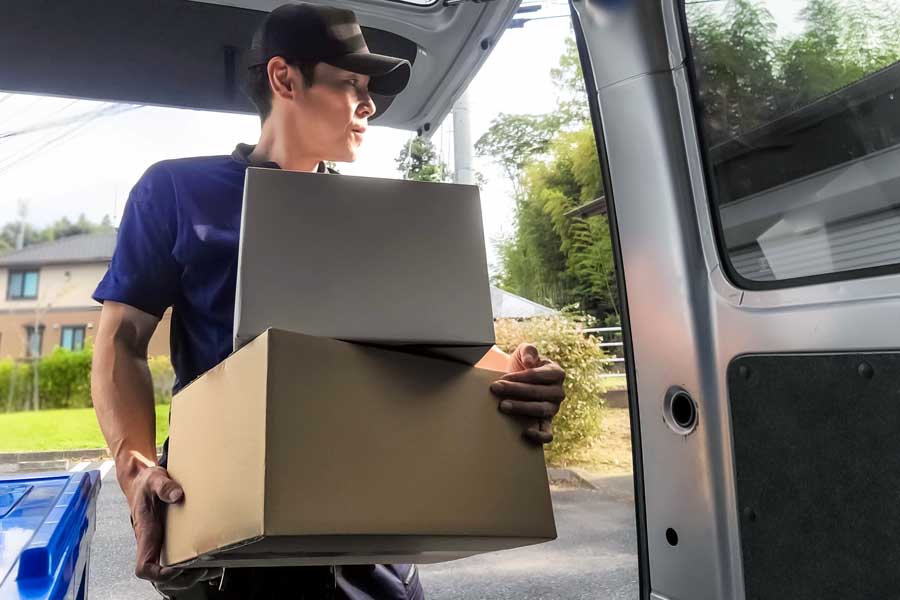 路上で荷物を運ぶ配送ドライバー（画像：写真AC）