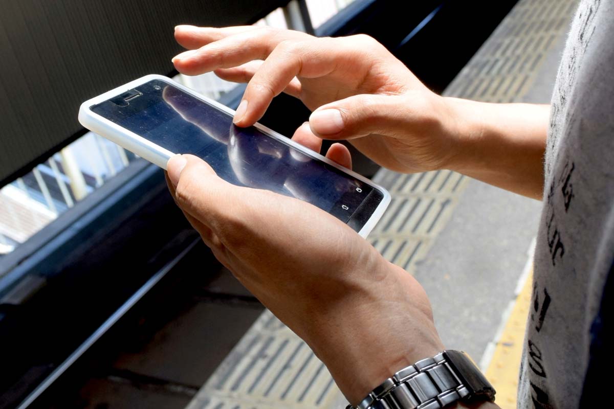 駅のホームでスマホを見る人のイメージ（画像：写真AC）