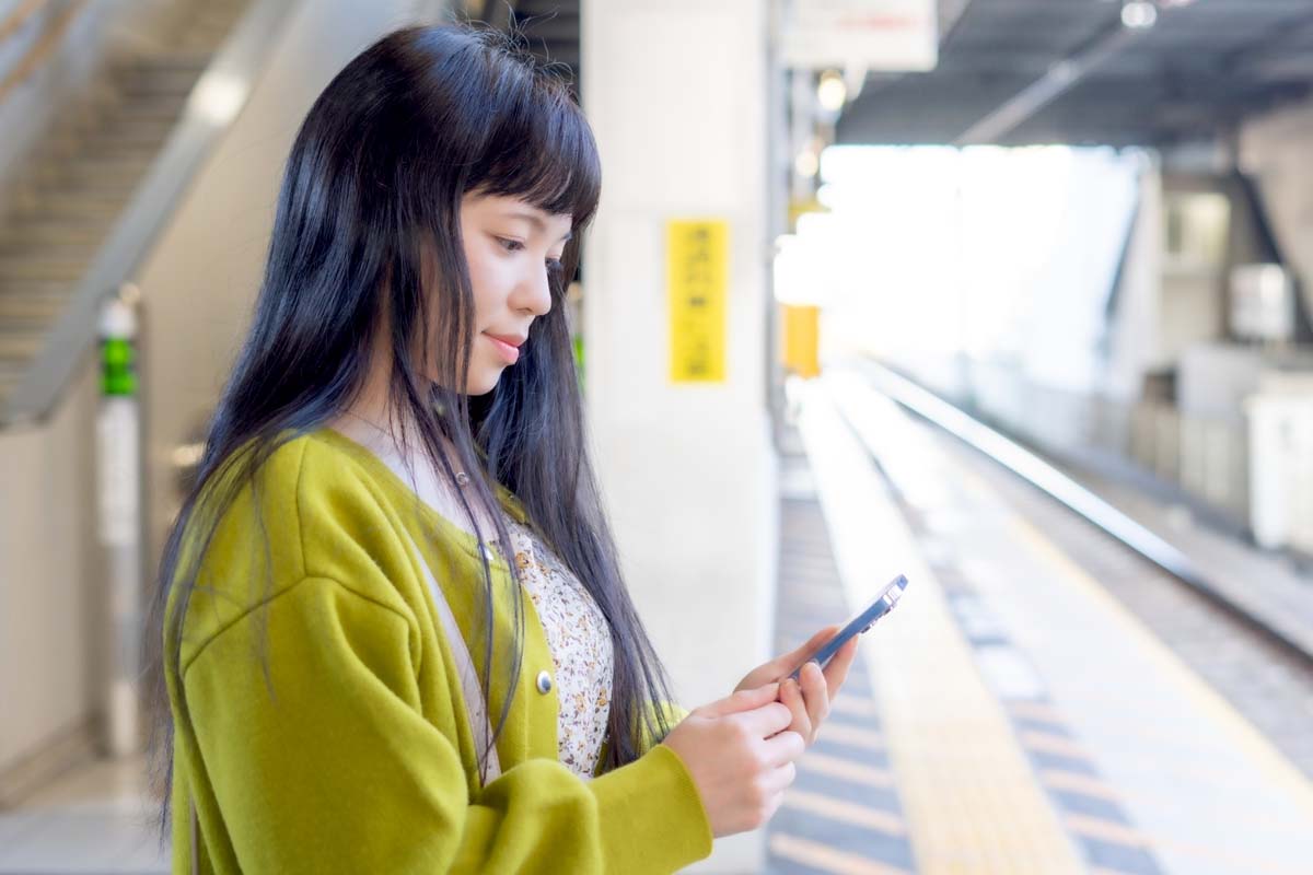 駅のホームでスマホを見る人のイメージ（画像：写真AC）